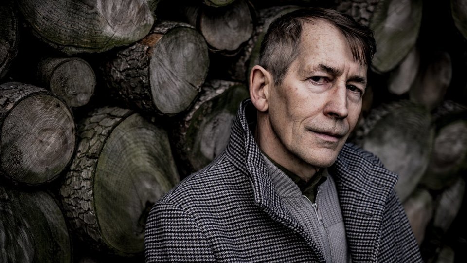 schrijver Chris De Stoop voor een stapel hout